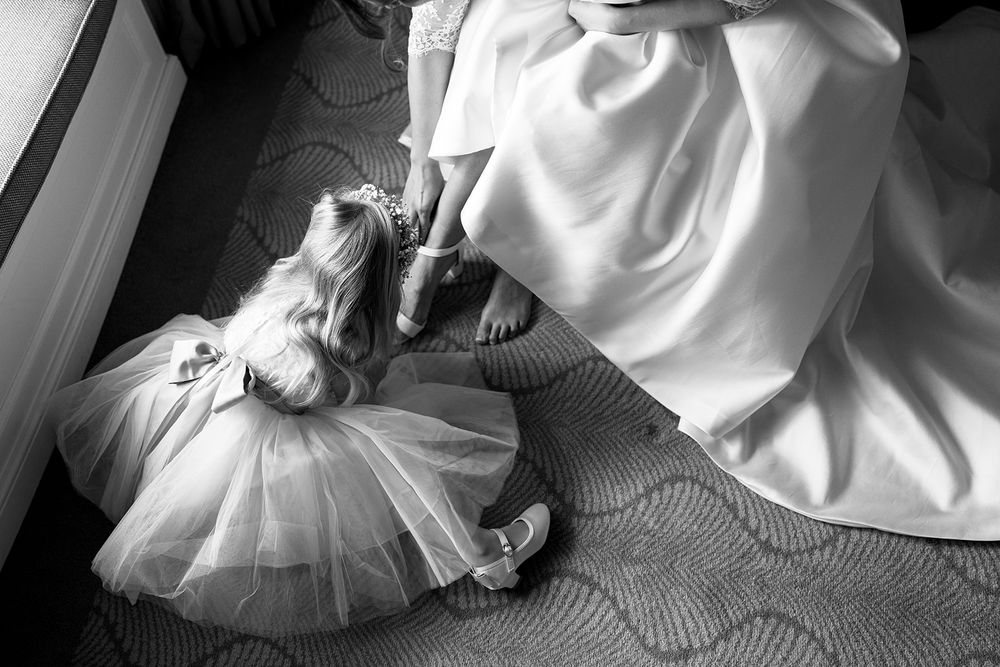 Black and white image of flowing wedding and flower girl dresses laying on textured carpet.