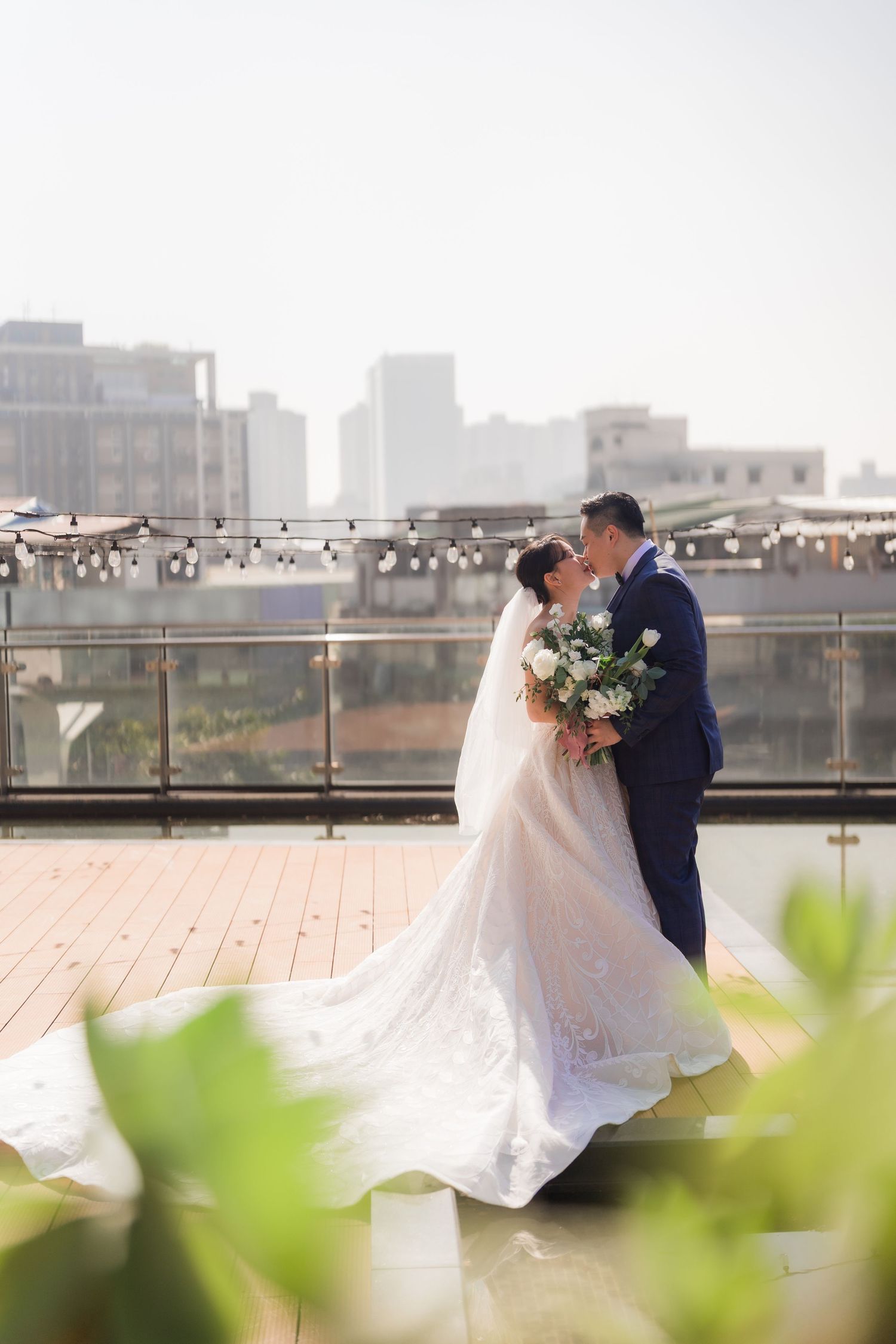 A romantic rooftop wedding ceremony with city skyline backdrop and string lights on a wooden deck.