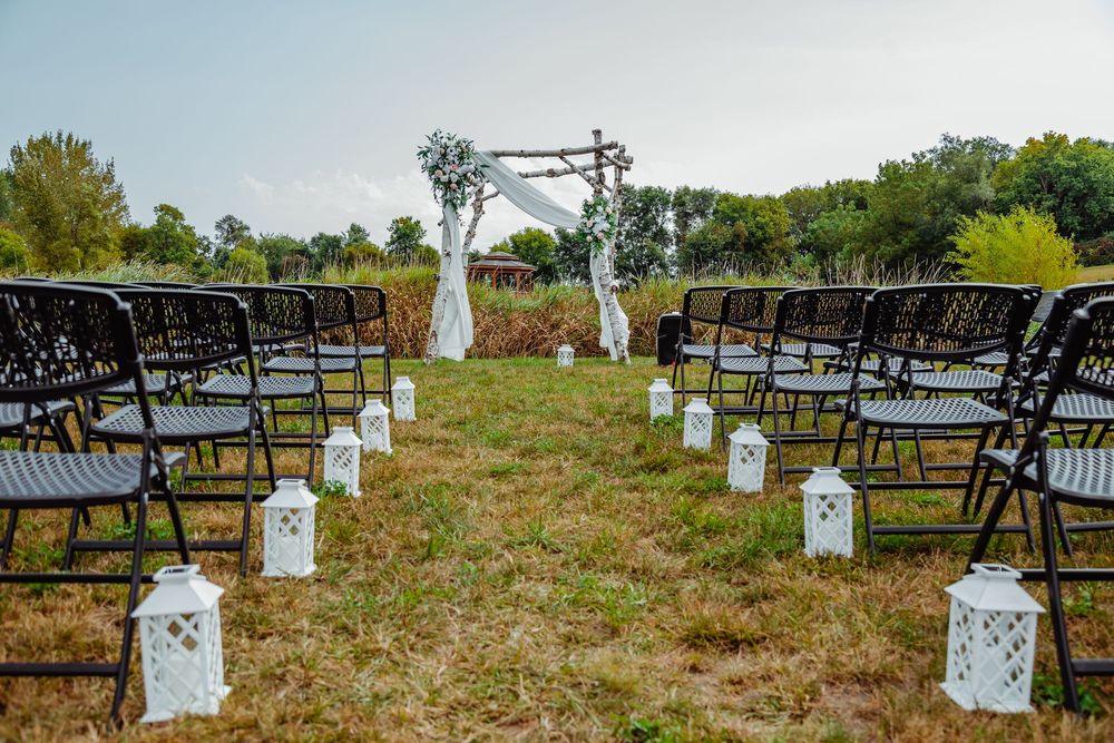 Row of weathered wooden chair frames on green grass with white canvas signs attached to metal poles.