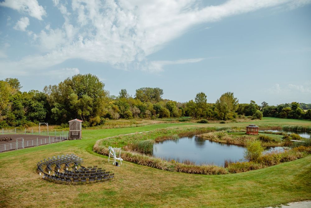 A panoramic view of a grassy shoreline with trees and a blue lake stretching across the horizon on a sunny day.