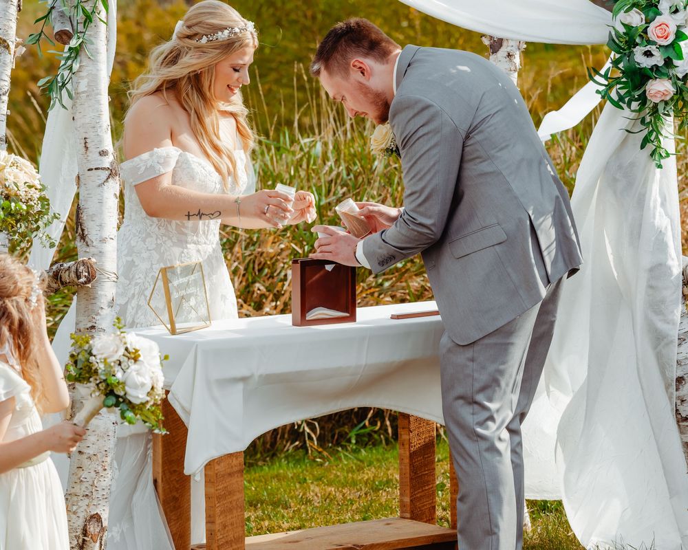 A couple exchanges rings during a scenic outdoor wedding ceremony surrounded by floral arrangements and mountain views.