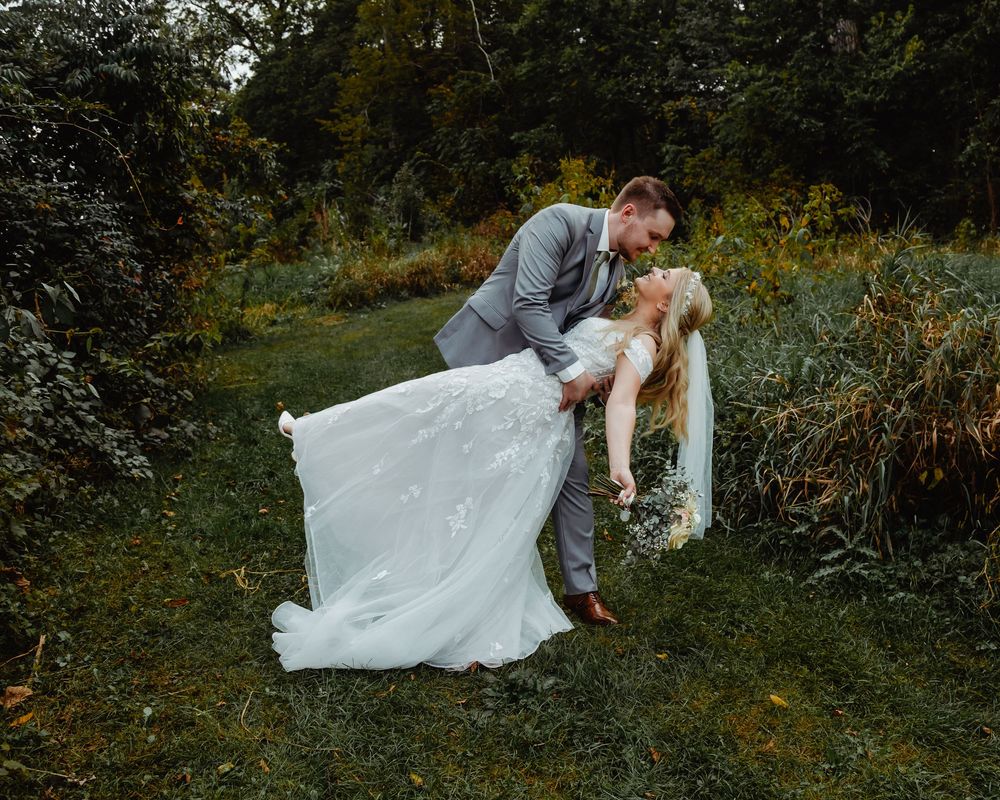A beautiful romantic moment captured outdoors in a forest setting with a flowing white wedding dress.