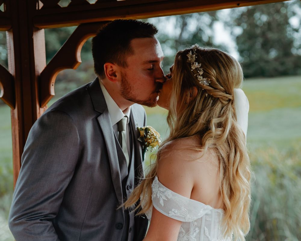 Two newlyweds share a romantic kiss during their outdoor wedding ceremony in a rustic venue.