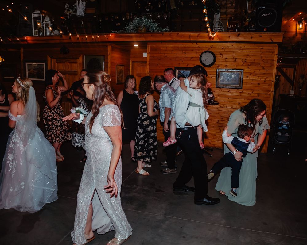 Wedding guests dancing on a dimly lit dance floor in a rustic wooden venue with string lights.