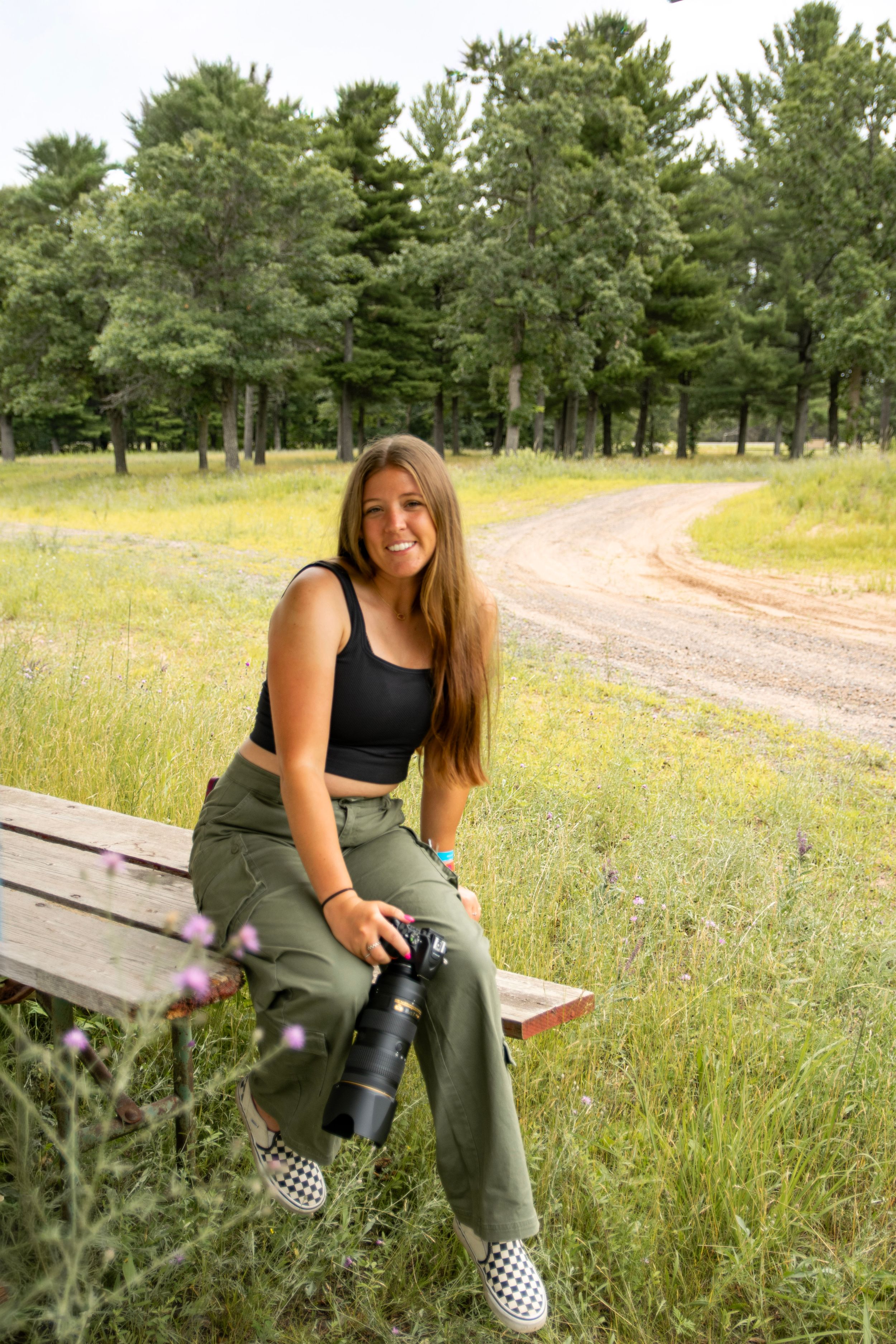 Photographer with camera sitting on wooden bench along rural dirt path.