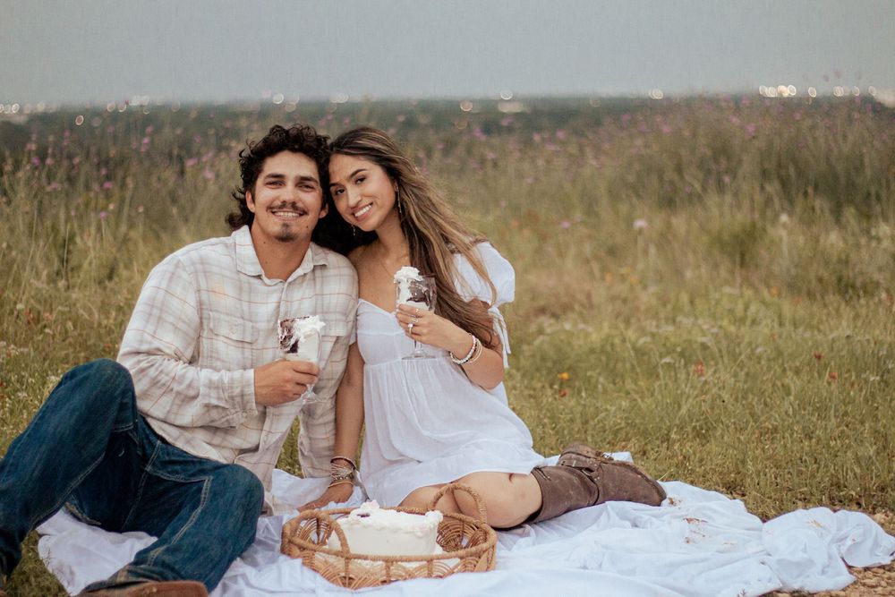 A couple enjoys a romantic picnic on a blanket in a grassy field on a sunny day.