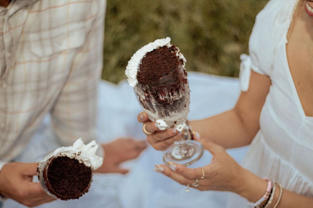 Two hands holding chocolate ice cream sundaes topped with whipped cream in glass goblets.