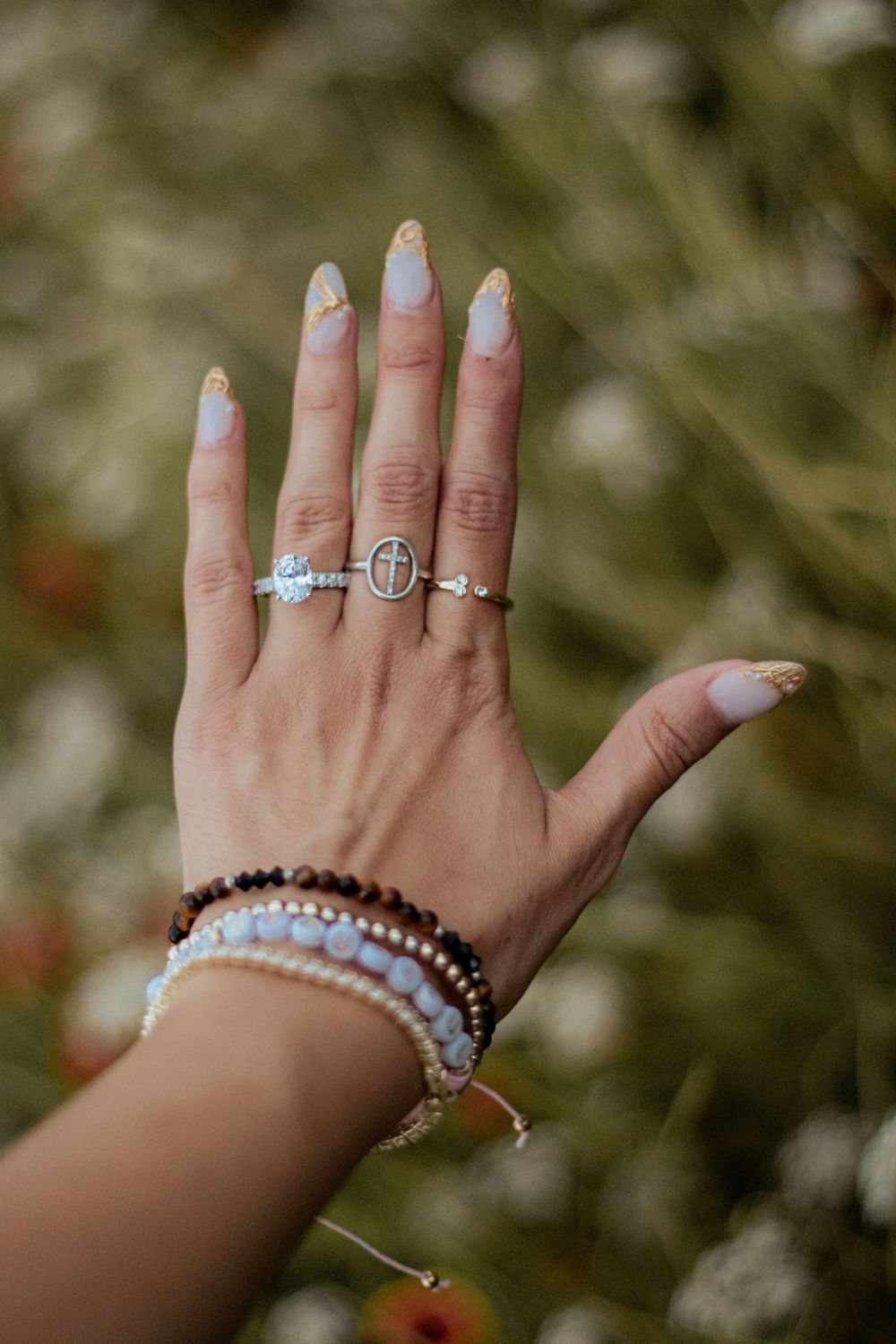 Close-up of hands wearing delicate rings and bracelets against a blurred natural background.