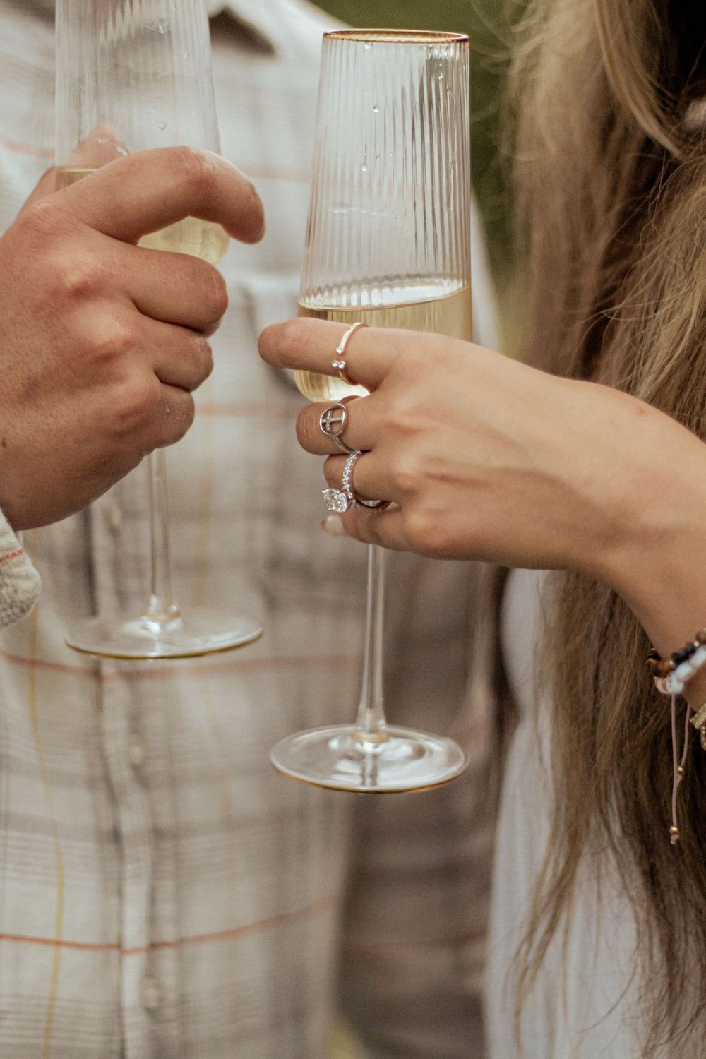 Two hands holding champagne flutes toast together as one person displays multiple elegant rings on their fingers.