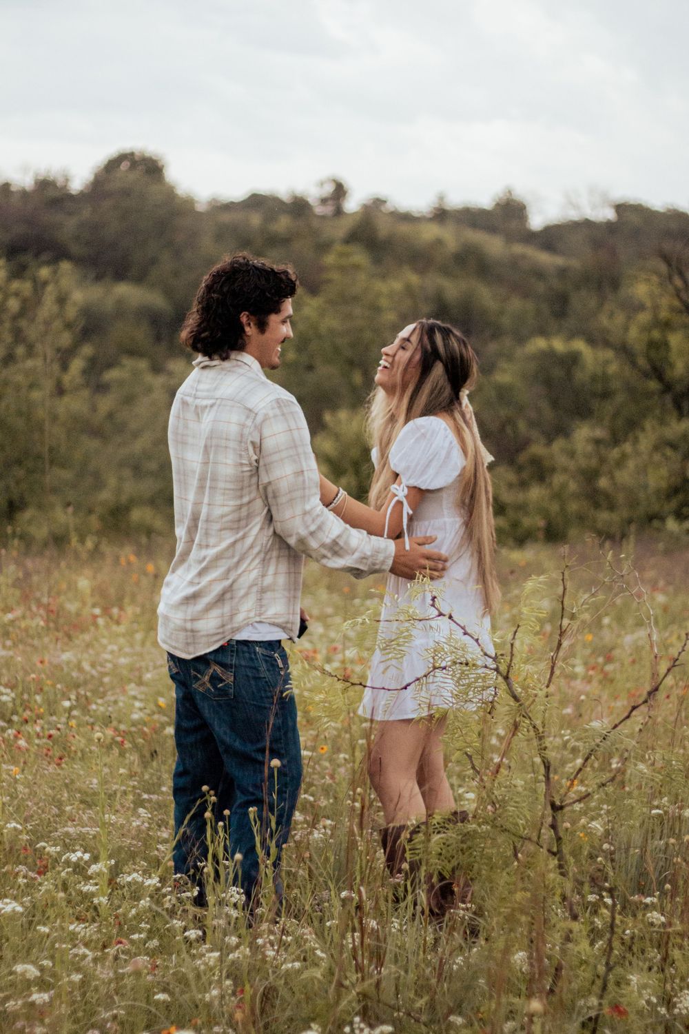 A couple share a joyful moment together in a wildflower meadow on an overcast day.
