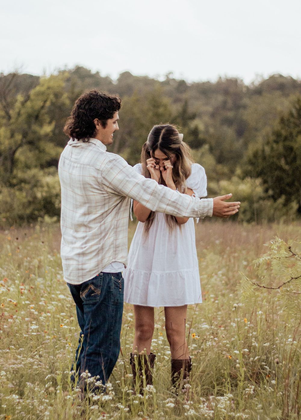 Two people share an emotional moment together in a sunlit field with wildflowers and trees in the background.