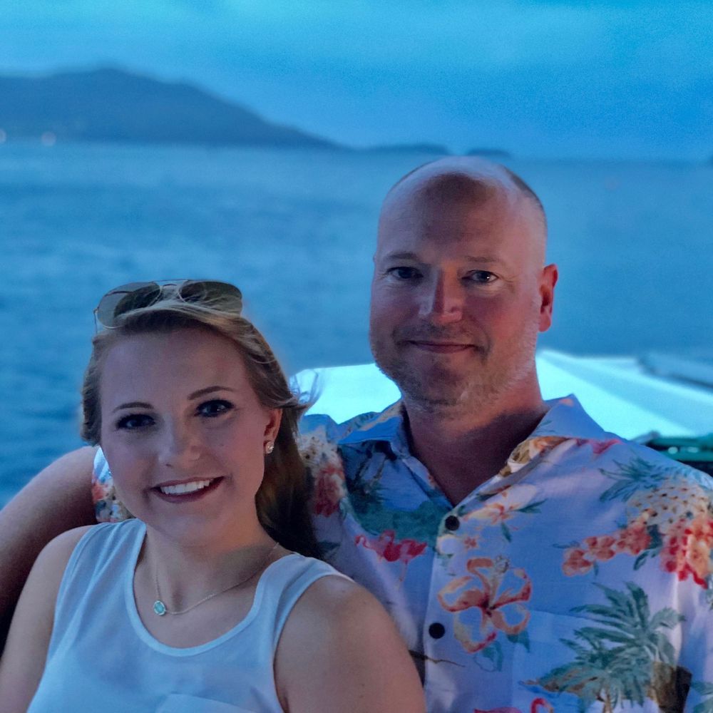 Couple poses outdoors with ocean view and Hawaiian tropical print attire in a series of casual photos with blue backdrop.