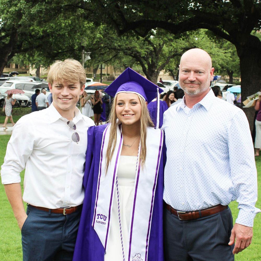 Graduate in purple cap and gown poses for photo outdoors during graduation ceremony.