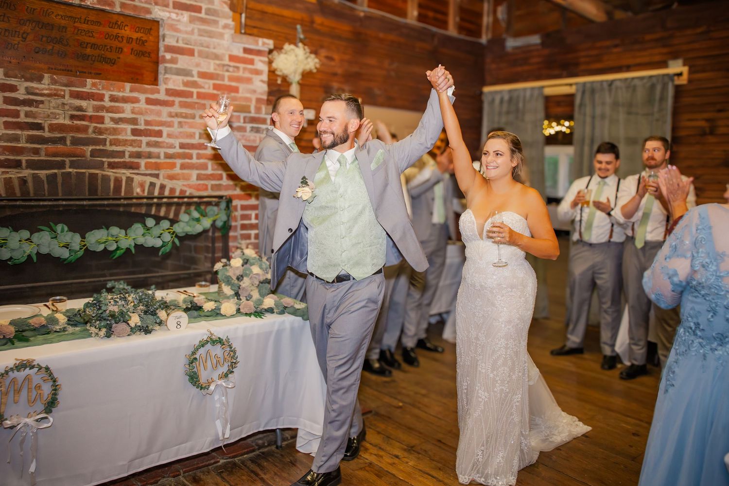 Newlyweds celebrate with raised arms during their first dance at a rustic brick-walled wedding reception venue.