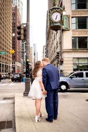 A couple shares intimate moments on a Chicago street corner with urban architecture surrounding them.