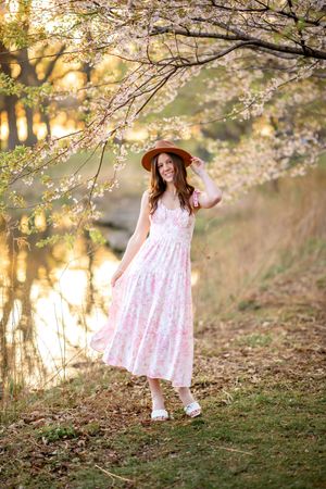 A pink dress twirls beneath blooming cherry blossom trees at sunset creating a dreamy spring scene.