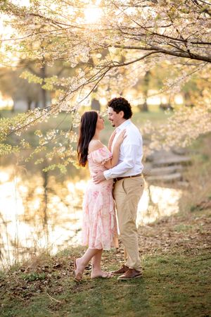 A romantic couple shares tender moments under blooming cherry blossom trees during a spring photoshoot at sunset.