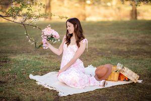 A picnic scene at sunset with a white blanket laid out on grass and a basket of flowers and refreshments.