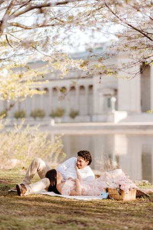 A couple relaxes on a grassy hill under blooming cherry blossom trees during springtime.
