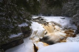 Rushing river water creates dramatic white rapids through a rocky gorge on a misty winter day.