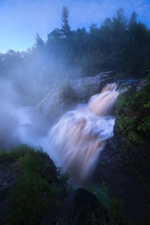 Scenic waterfall cascades through misty forest landscape during blue hour.