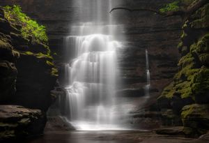 A majestic waterfall cascades down moss-covered rocks in a dark forest setting, creating a dreamy ethereal atmosphere.