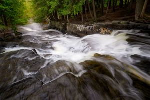 Rushing white water cascades over smooth rocks in a lush forest stream creating dramatic long exposure effects.