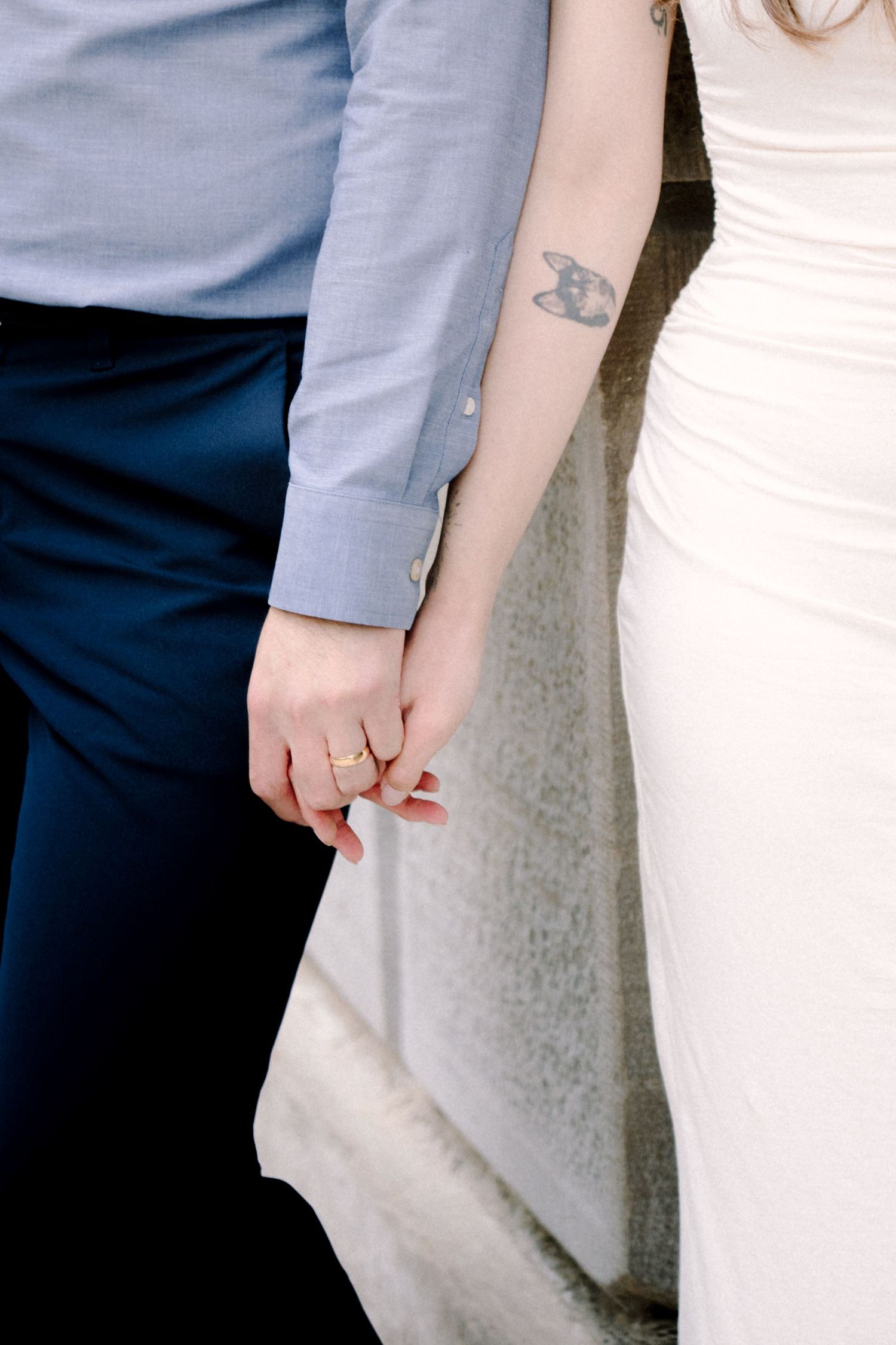 Close up of couple holding hands showing wedding ring and small tattoo detail.