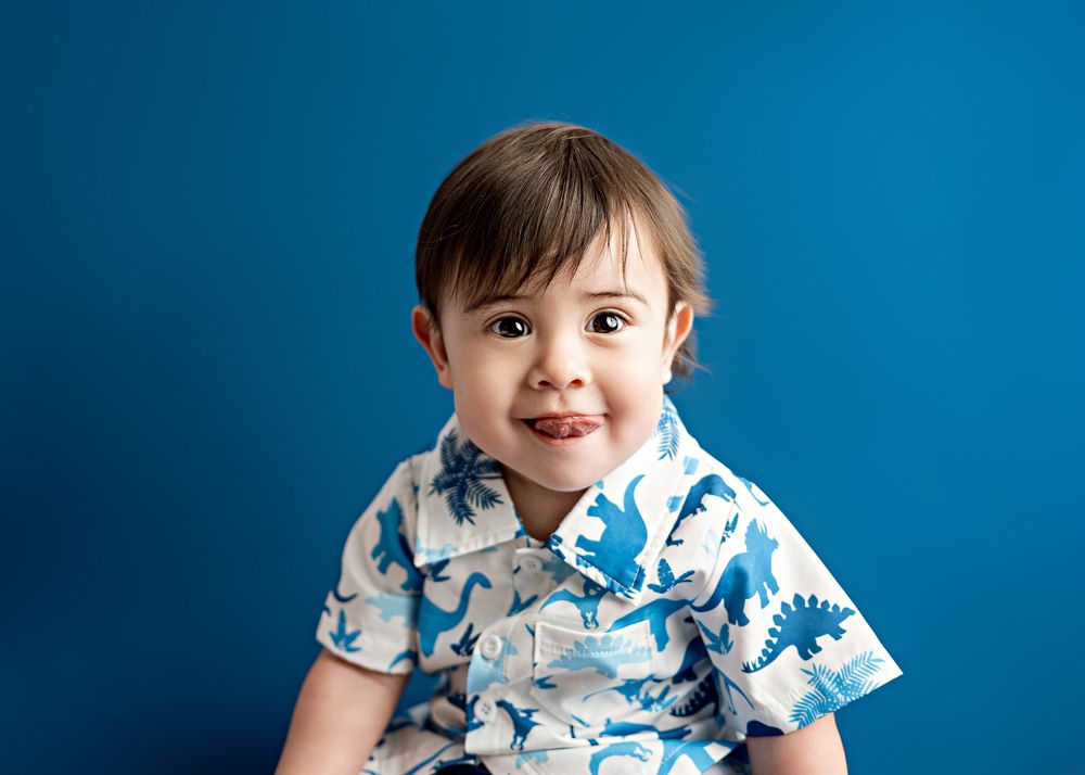 Cheerful toddler wearing a short-sleeved white shirt with blue floral print against a bright blue background.