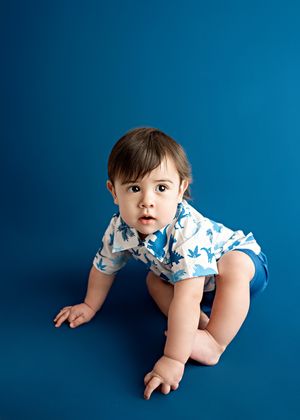 A toddler wearing a blue and white patterned shirt crawls against a deep blue background.