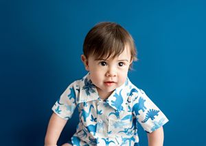 Baby wearing blue and white dinosaur print shirt poses against bright blue backdrop.