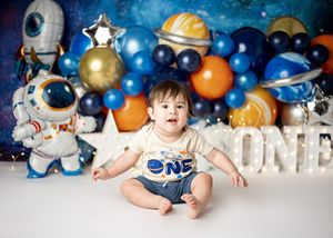 Space-themed first birthday party setup with astronaut decorations and colorful planet balloons against a blue backdrop.
