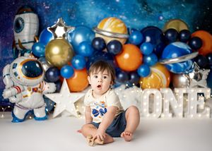Space themed first birthday photo setup with balloons in blue, orange and gold against a starry backdrop.