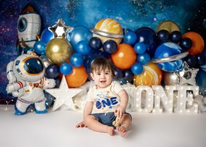 Space-themed first birthday party setup with astronaut decorations, blue and orange balloons, and ONE lettering against starry backdrop.