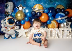Outer space themed first birthday photo setup with astronaut decorations, stars and colorful balloon display.