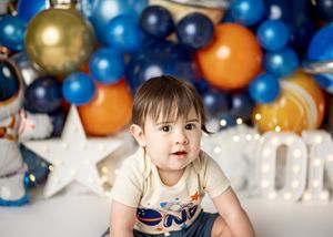 Festive birthday party setup with blue and gold balloon garland backdrop, white stars and cushions on the floor.