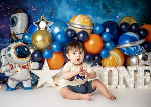 Navy blue and metallic balloon arch with outer space decorations and planets creates a celestial first birthday theme.