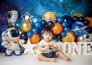 A space-themed birthday party setup with astronaut decorations, colorful balloons and letter ONE against a starry backdrop.