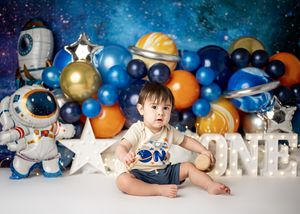 Space themed first birthday party setup with astronaut decorations, blue and orange balloons, and stars against a galaxy backdrop.