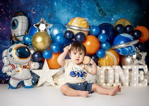Outer space themed first birthday photo setup with balloons, astronaut decorations, and white letters spelling ONE.