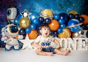 Baby lays between colorful shiny Christmas ornaments and holiday lights, creating a festive holiday photo scene.