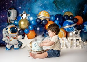 Baby wearing navy blue outfit lying on white floor next to holiday decorations in blue and silver tones.