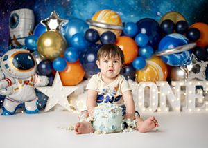 Space themed first birthday party setup with astronaut decorations and blue and gold balloon garland backdrop.