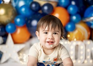 Baby lying on floor at party with blue and orange balloons and silver star decorations in background.