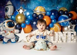 First birthday cake smash photo session with space theme decorations including balloons, stars, and astronaut balloons.