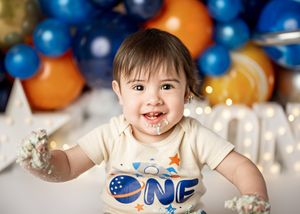 Festive birthday party setup with blue and orange balloons, white decor, and a "ONE" themed celebration outfit.