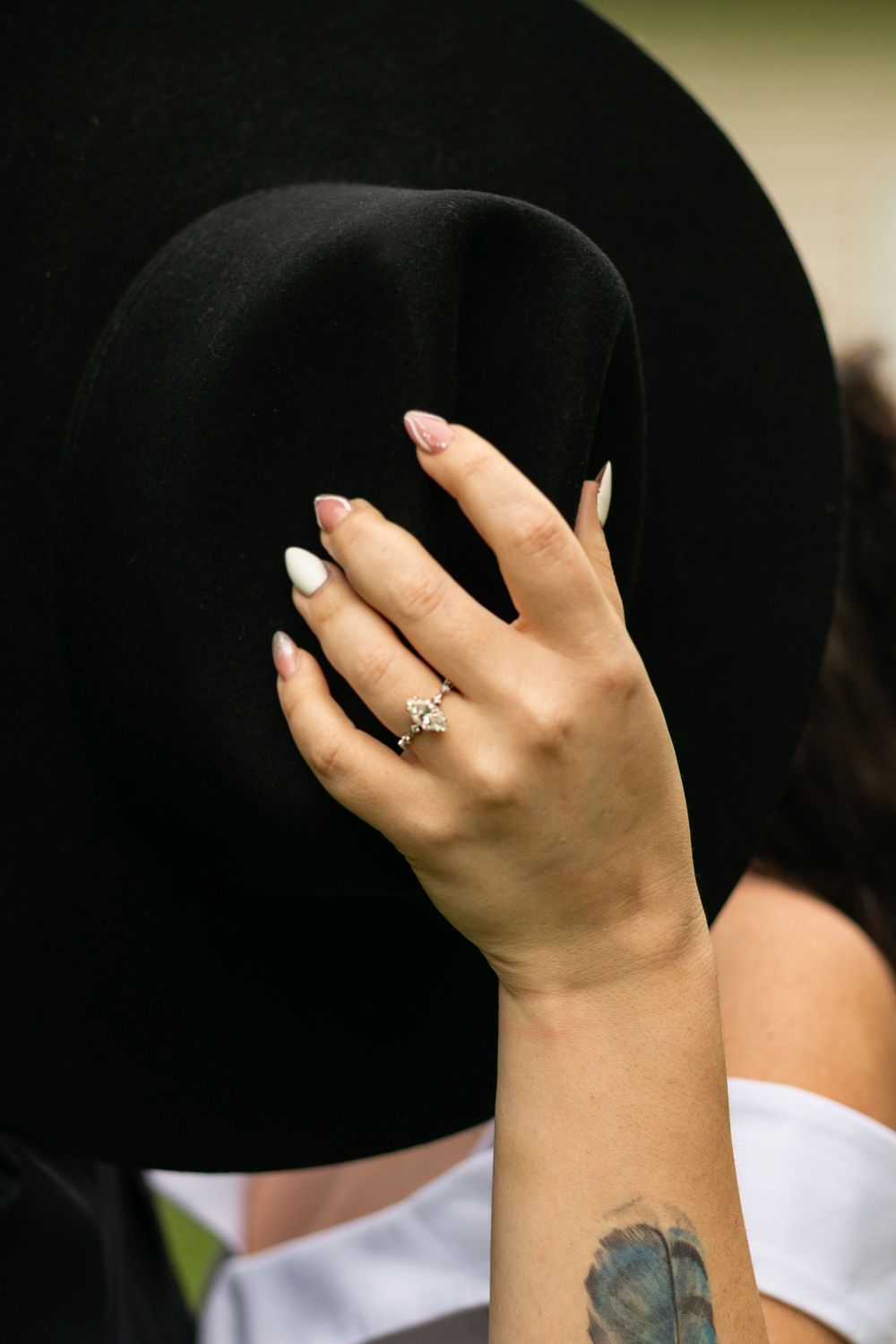 A close-up view of a hand wearing a ring extends towards a black hat against a blurred background.