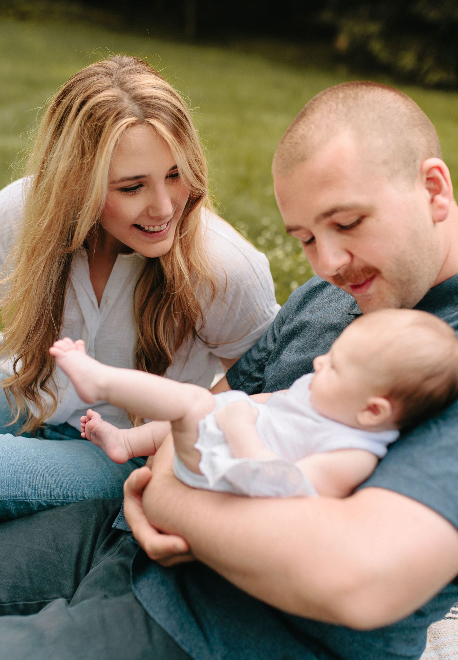 A loving family moment outdoors as parents bond with their baby on a sunny day in the grass.
