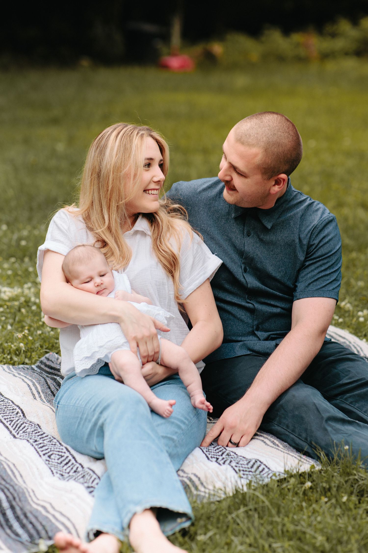 Family relaxes together on a striped blanket in the grass on a sunny summer day.