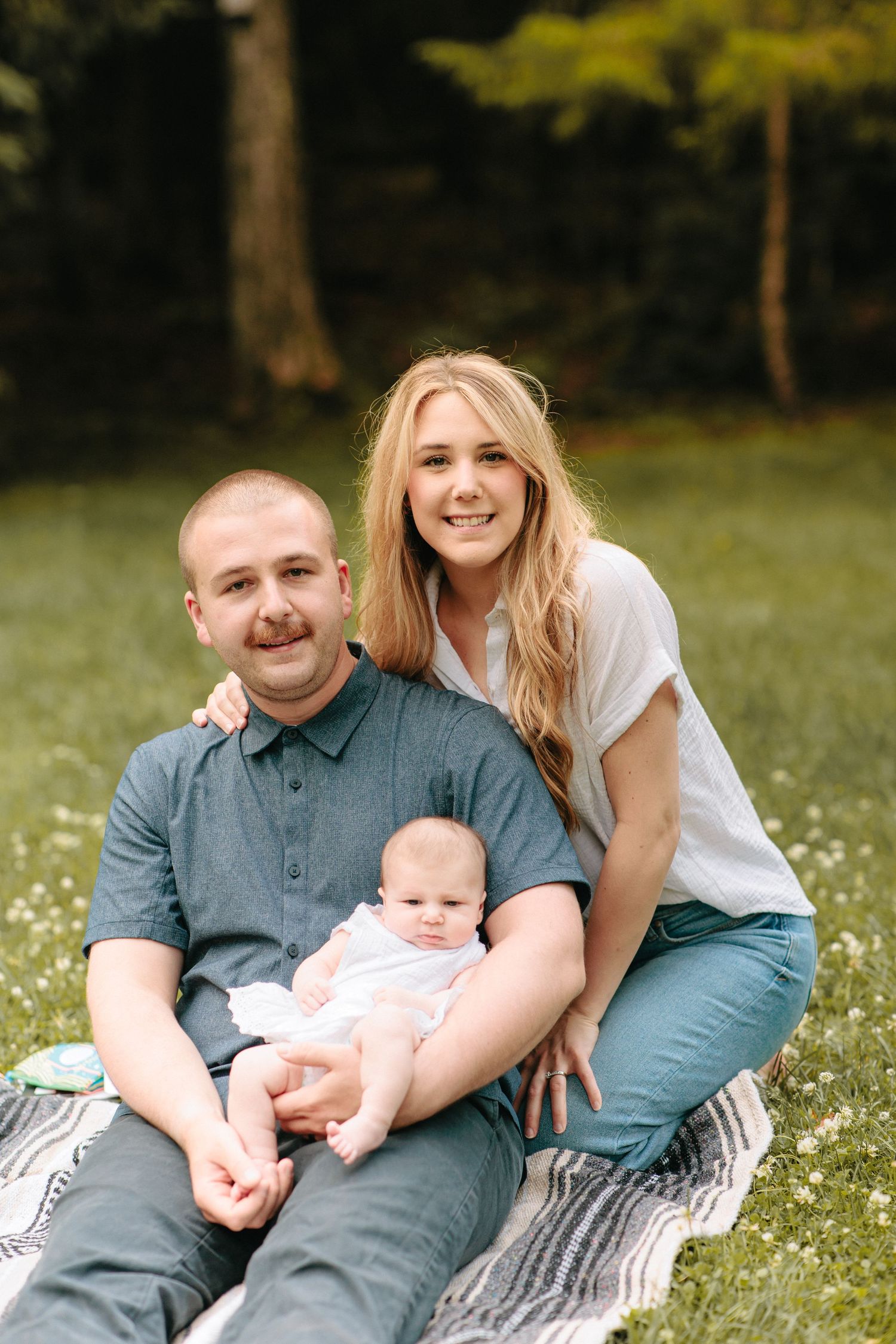 A family poses together on a blanket in a wildflower meadow during a sunny outdoor photoshoot.